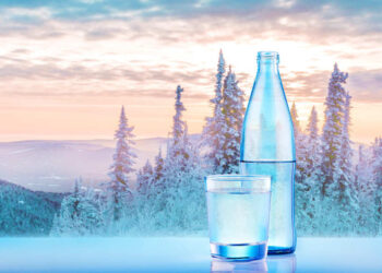 Wasserflasche und Glas vor winterlicher Gebirgslandschaft