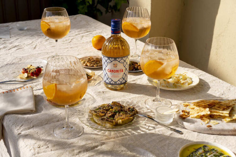 Eine Flasche Canonita de Mallorca und vier Gläser auf einem Tisch mit kleinen Snacks