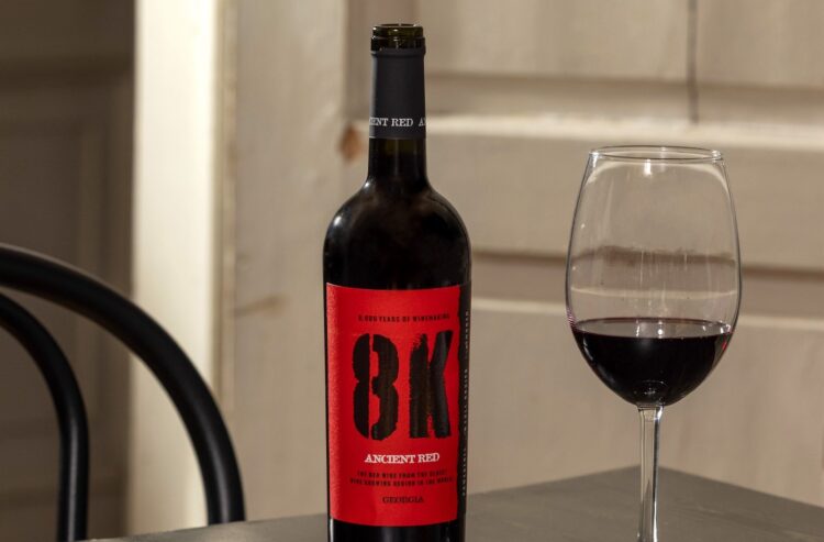 Eine Flasche 8K Ancient Red und ein Weinglas auf einem Tisch