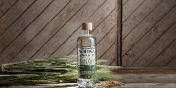 Koskenkorva-Flasche mit Getreide-Ähren vor Holzwand