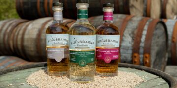 drei verschiedenen Flaschen Kingsbarns, im Hintergrund Whiskyfässer