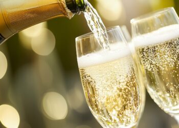 Sekt wird aus Flasche in zwei Gläser geschenkt