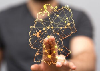 Durchsichtige Deutschlandkarte mit vielen Ortspunkten, die durch Linien verbunden sind, im Hintergrund unscharf ein Mann, der seine Hand auf die Karte legt