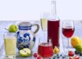 Stillleben mit Apfelwein-Bembel, einer Flasche mit rotem Fruchtwein, verschiedenen Gläsern mit Apfel- und Fruchtweinen und dekorativen Früchten