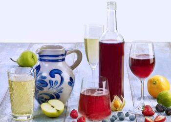 Stillleben mit Apfelwein-Bembel, einer Flasche mit rotem Fruchtwein, verschiedenen Gläsern mit Apfel- und Fruchtweinen und dekorativen Früchten