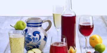 Stillleben mit Apfelwein-Bembel, einer Flasche mit rotem Fruchtwein, verschiedenen Gläsern mit Apfel- und Fruchtweinen und dekorativen Früchten