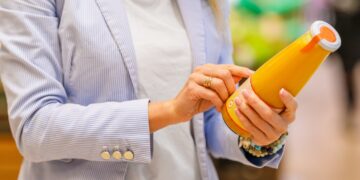 Frau im Supermarkt liest Etikett auf einer Saftflasche