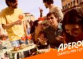 Aperol-Werbemotiv: Lebhafte Szene auf einer italienischen Piazza, junge Leute trinken Aperol Spritz