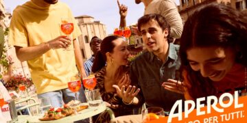 Aperol-Werbemotiv: Lebhafte Szene auf einer italienischen Piazza, junge Leute trinken Aperol Spritz