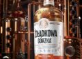 Eine Flasche des Kräuterlikörs von Żołądkowa Gorzka, im Hintergrund Brennblasen in einer Destillerie