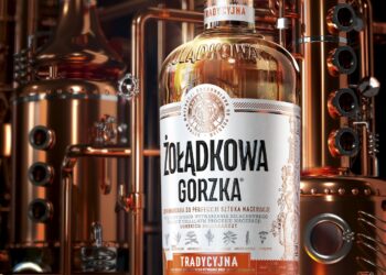 Eine Flasche des Kräuterlikörs von Żołądkowa Gorzka, im Hintergrund Brennblasen in einer Destillerie