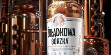 Eine Flasche des Kräuterlikörs von Żołądkowa Gorzka, im Hintergrund Brennblasen in einer Destillerie
