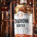 Eine Flasche des Kräuterlikörs von Żołądkowa Gorzka, im Hintergrund Brennblasen in einer Destillerie