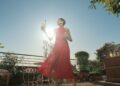 Ausschnitt aus dem neuen Werbespot: junge Frau in rotem Kleid mit Lilletflasche auf einer sonnigen Terrasse
